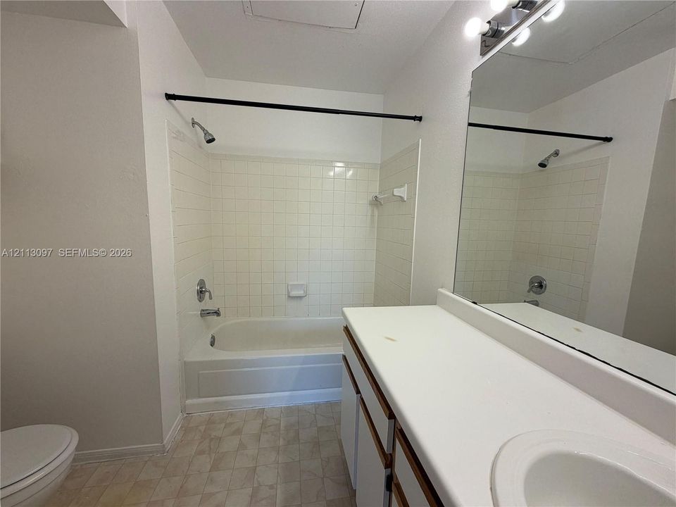 Bathroom featuring a combination bathtub and shower with white wall tile, a large wall-mounted mirror, vanity with a white countertop and integrated sink, and an overhead vanity light fixture