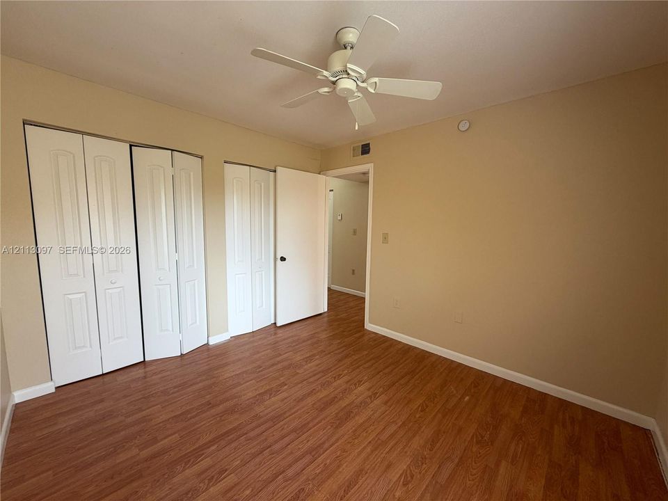 Room featuring wood-finish flooring, dual bi-fold door closets, and a ceiling fan