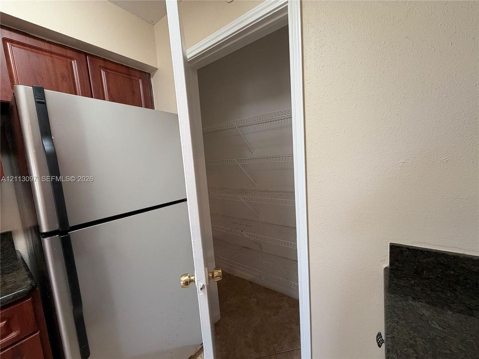Pantry featuring white wire shelving and tile flooring, positioned near cabinetry with dark-finish doors and stone-style countertops