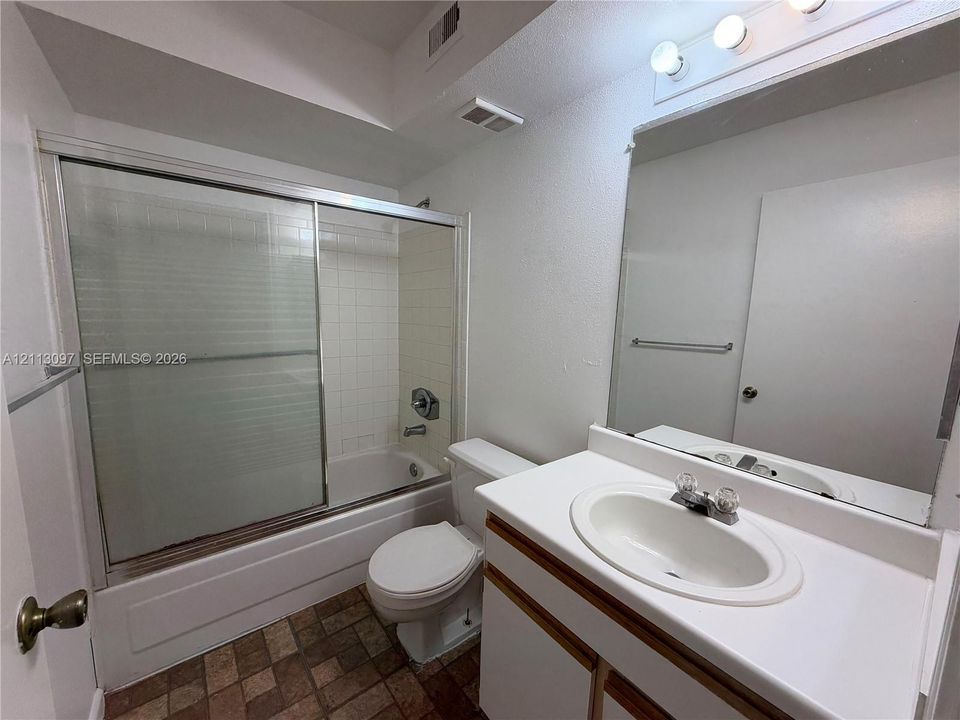 Bathroom featuring a vanity with a white countertop and oval basin, a shower-tub combination with sliding glass doors, tile-surround shower walls, and a large wall-mounted mirror with integrated lighting