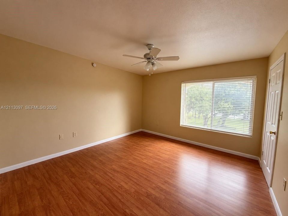Room featuring wood-finish flooring, a ceiling fan with integrated lighting, a large window with horizontal blinds, and a six-panel door