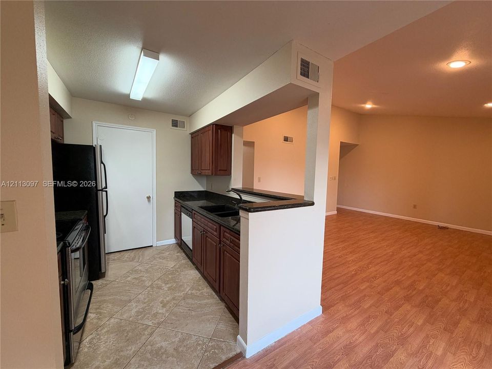 Kitchen featuring dark-toned cabinetry, stone-finish countertops, tile flooring, and integrated black appliances