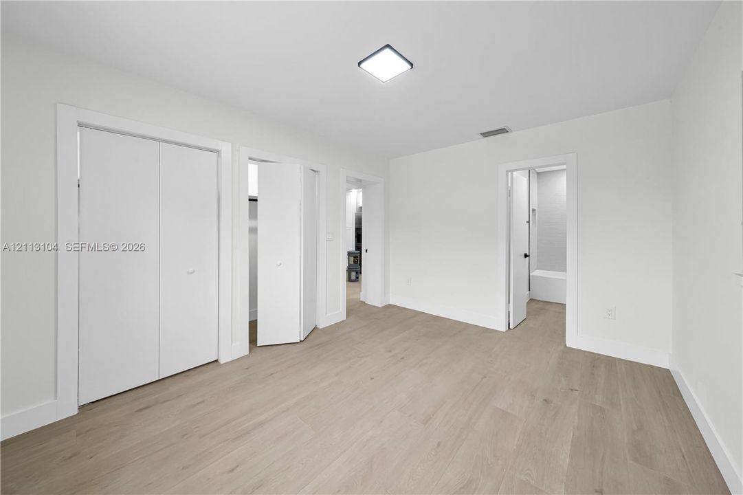 Neutral-toned wood-finish flooring, two sets of white bi-fold closet doors, square flush-mount ceiling lighting, and crisp white wall finishes