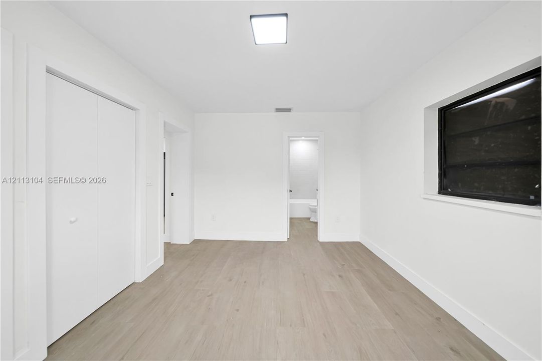 Neutral interior featuring wood-finish flooring, white walls, built-in double-door closet, and square flush-mount lighting