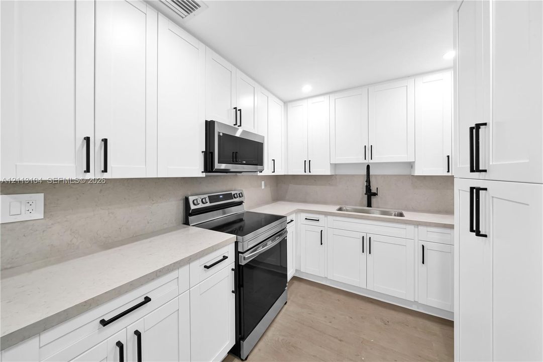 Kitchen featuring shaker-style white cabinetry, stone-finish countertops, matte black hardware, stainless steel appliances, and wood-finish flooring