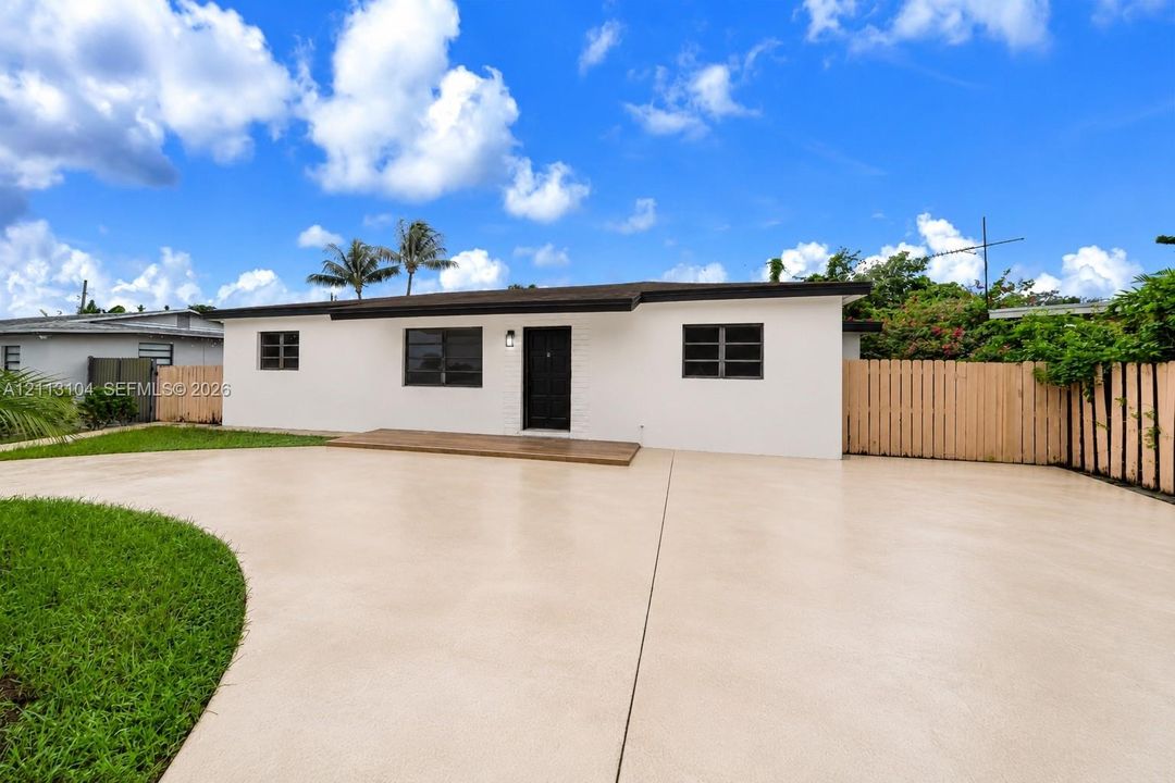 Exterior featuring smooth stucco siding, wide concrete driveway, wooden front deck, black-framed windows, and a privacy fence