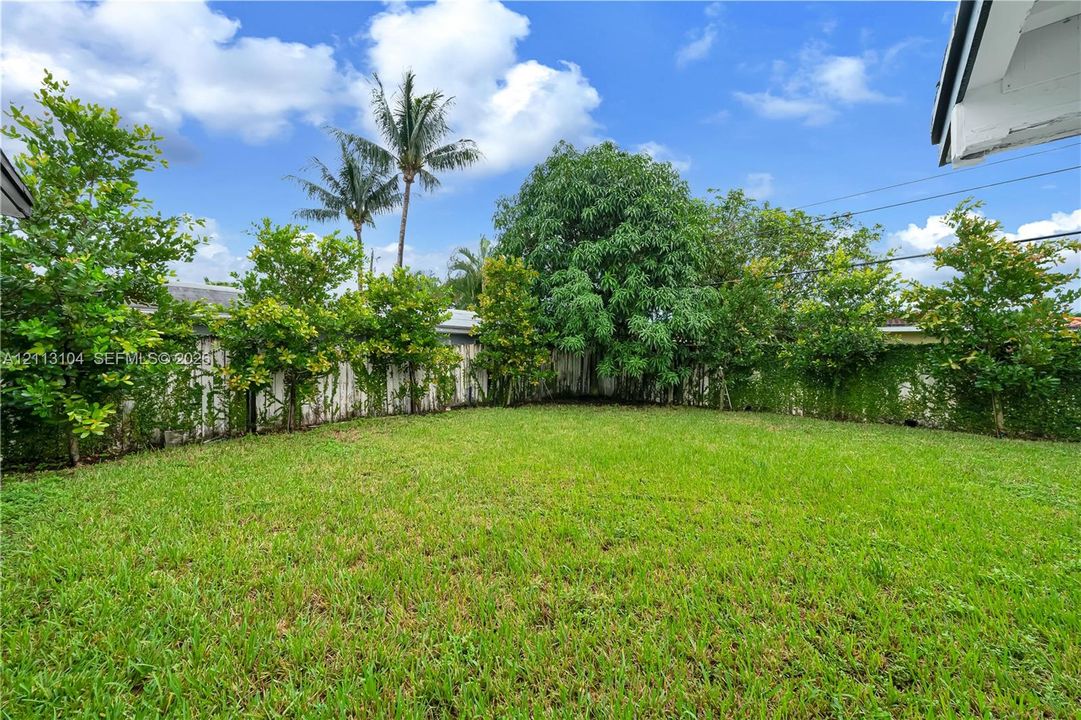 Private backyard featuring an expansive lawn, established perimeter trees, and a full-height privacy fence