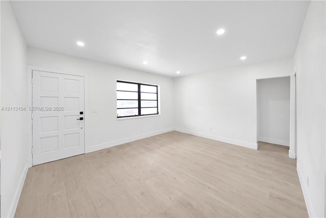 Neutral interior featuring wood-finish flooring, recessed lighting, white walls, a grid-pattern window with black framing, and a six-panel door with matte black hardware