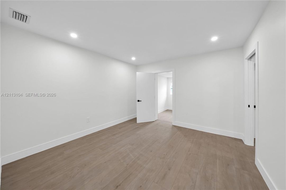 Interior room featuring neutral wall paint, wood-finish flooring, recessed lighting, and doors with matte black hardware