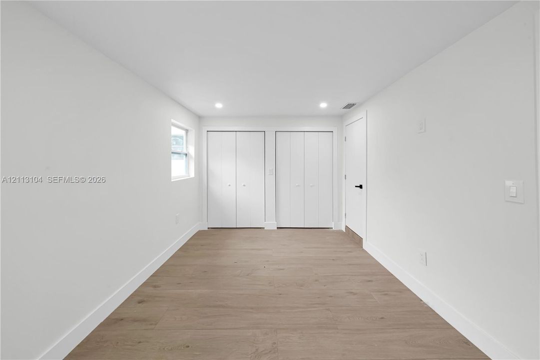 Interior space featuring wood-finish flooring, two sets of white bi-fold closet doors, recessed ceiling lighting, and a single window