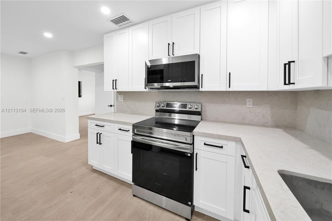Kitchen featuring white shaker-style cabinetry, stone-surface countertops, stainless steel appliances, and wood-finish flooring