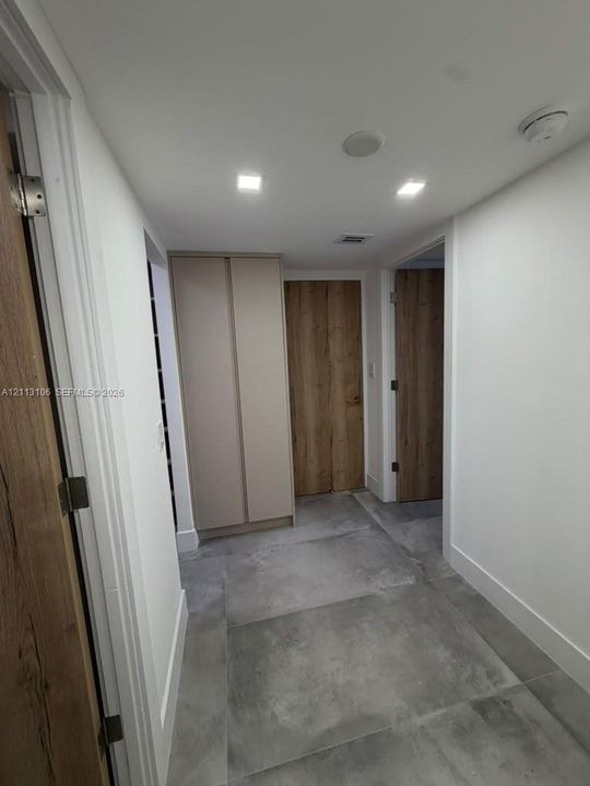 Hallway featuring large-format tile flooring, recessed ceiling lighting, wood-finish interior doors, and built-in floor-to-ceiling cabinetry
