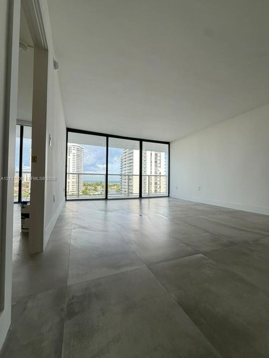 Open-concept room featuring large-format tile flooring, floor-to-ceiling glass wall, and attached balcony with metal railing