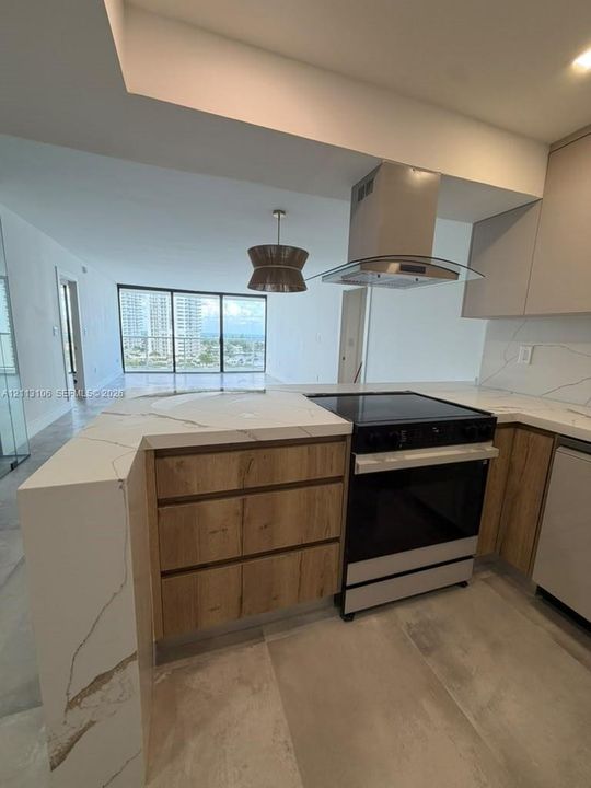 Kitchen featuring waterfall stone countertops, wood-finish cabinetry, a stainless steel range with a glass-canopy vent hood, and large-format tile flooring