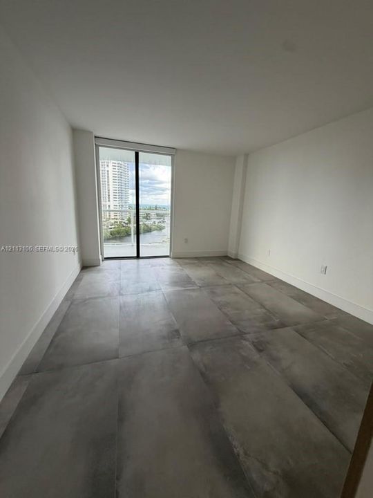 Interior room featuring large-format grey tile flooring, neutral wall finishes, and floor-to-ceiling glass sliding doors opening to a balcony