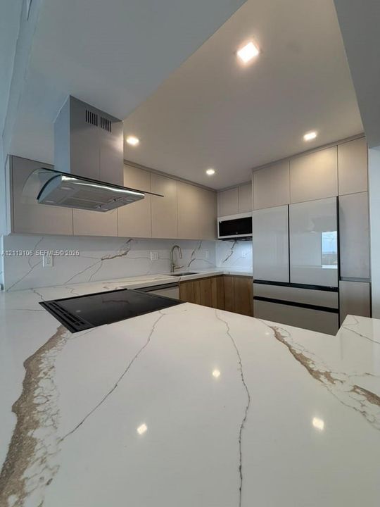 Kitchen featuring stone-finish countertops with waterfall edge, full-height stone-finish backsplash, flat-panel cabinetry, stainless steel range hood, and recessed lighting
