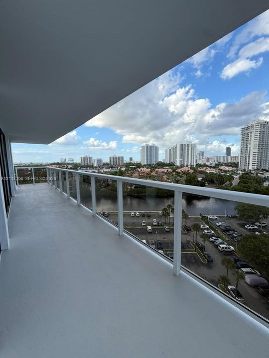 Covered balcony featuring a white railing and glass panels, overlooking the cityscape and water