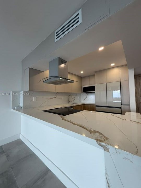 Kitchen featuring a waterfall-edge stone countertop with veining, flat-panel cabinetry, stainless steel range hood, built-in appliances, and recessed lighting