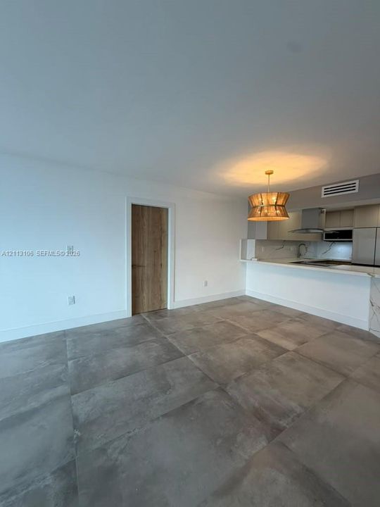Large-format stone-finish floor tiles, custom wood-finish interior door, kitchen peninsula with waterfall stone countertop, integrated cabinetry, and decorative drum pendant light fixture