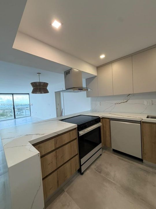 Kitchen featuring stone-finish countertops with waterfall edge, veined backsplash, two-tone flat-panel cabinetry, stainless steel range with overhead vent hood, and large-format tile flooring
