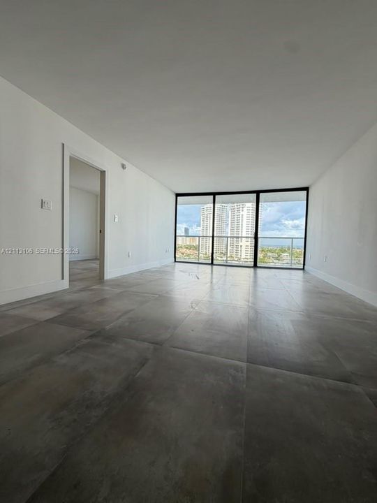 Large-format tile flooring, floor-to-ceiling glass panel windows, and balcony access with a metal railing