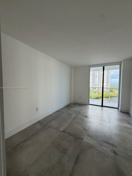 Interior space featuring large-format grey tile flooring, neutral wall finishes, and a sliding glass door providing access to a private balcony