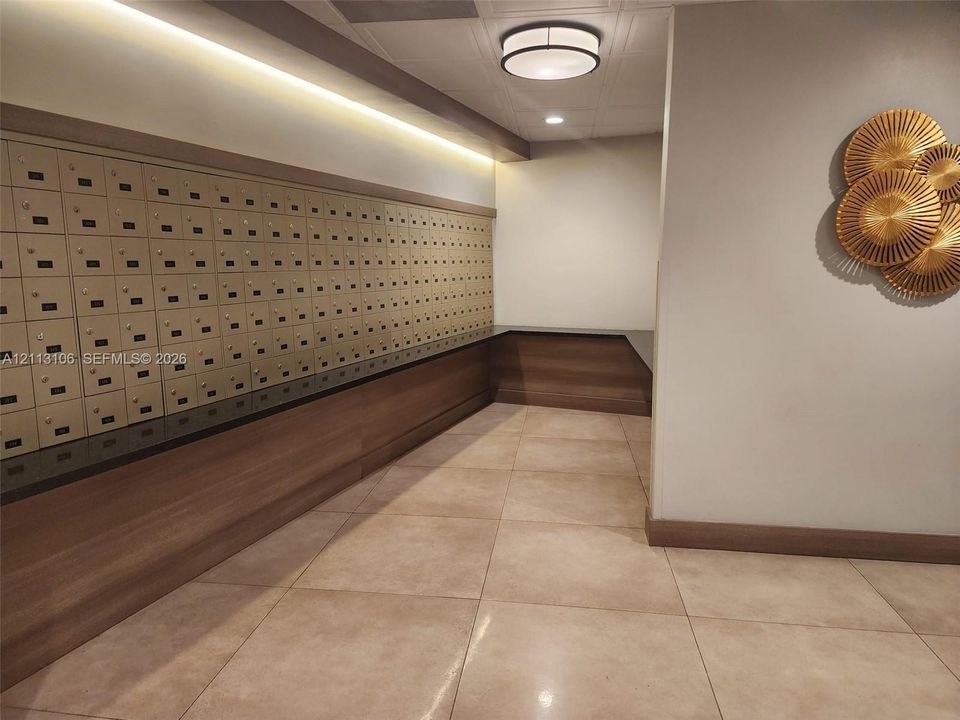 Secure lobby featuring a wall of built-in metal mailboxes, porcelain tile flooring, wood-finish paneling, and recessed linear lighting