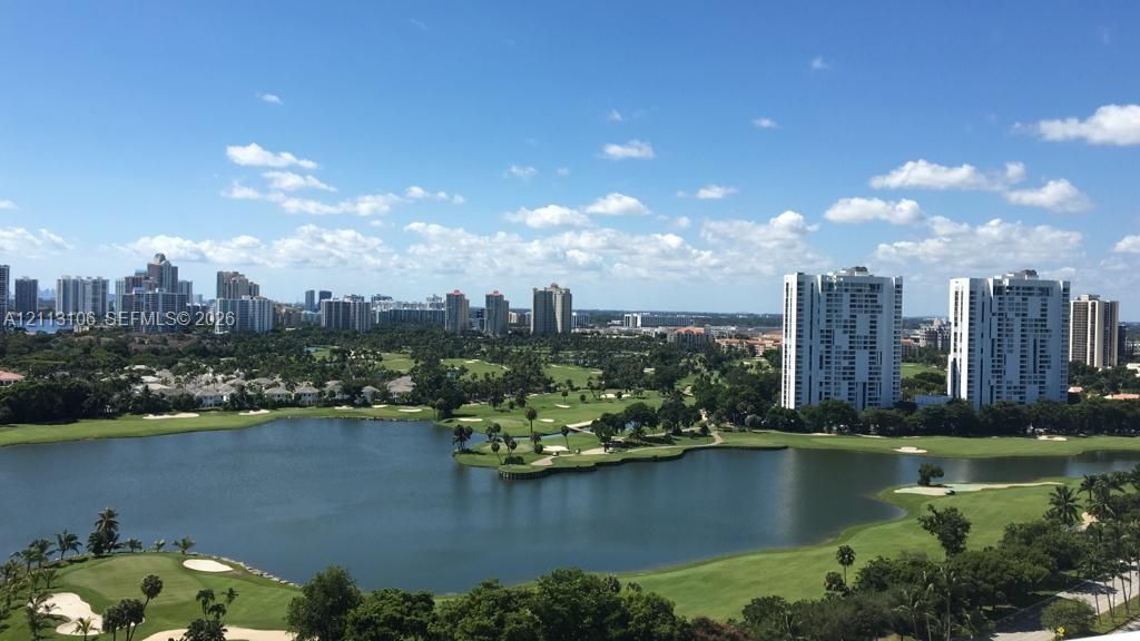 High-rise perspective featuring a sprawling golf course, expansive lake, manicured greenery, and urban skyline
