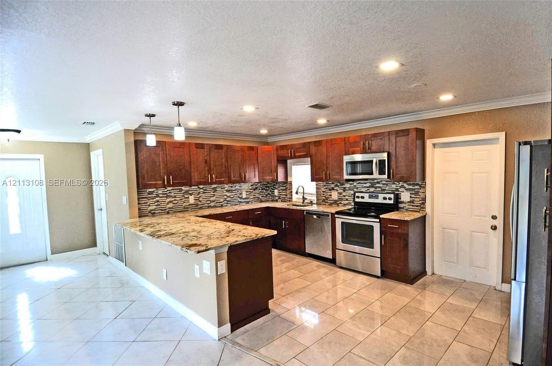 Kitchen featuring stone-patterned countertops, wood-finish cabinetry, a decorative tile backsplash, recessed lighting, and stainless steel appliances
