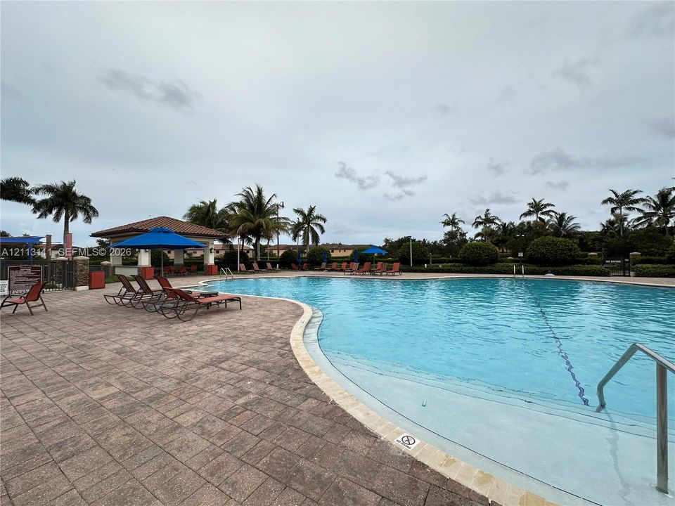 Community swimming pool featuring a concrete paver deck, built-in structural pavilion, and metal handrail entry