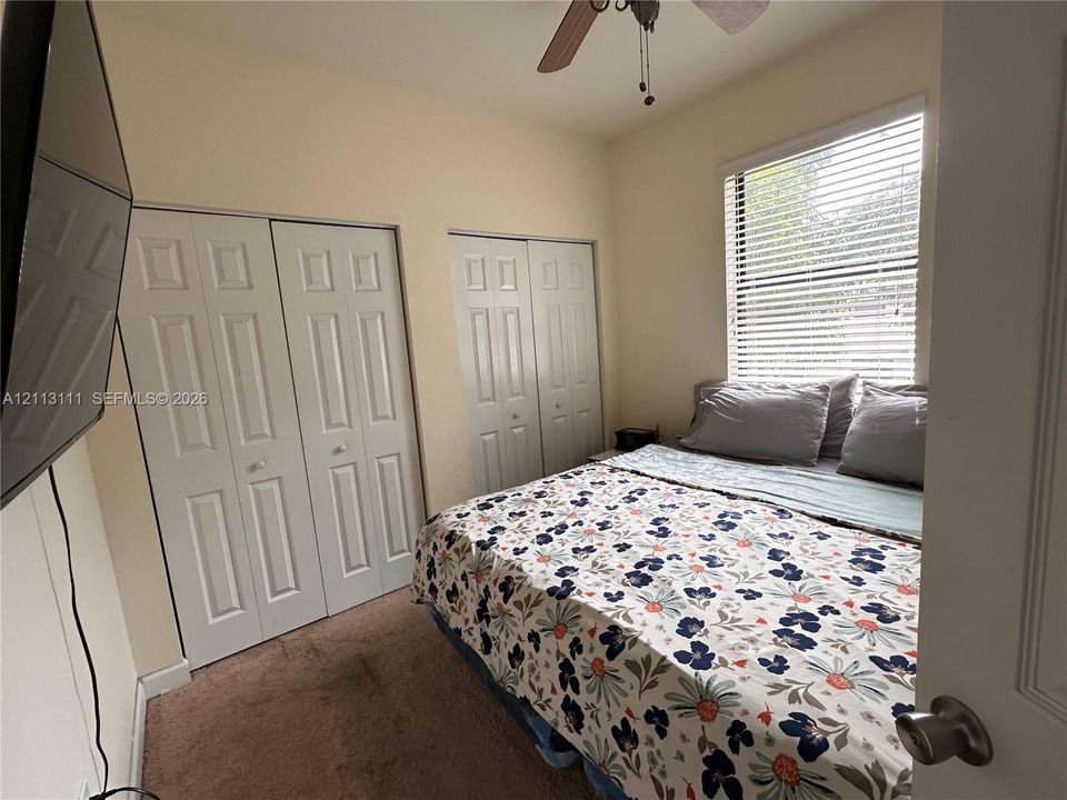 Room featuring neutral wall paint, two sets of bifold closet doors, carpeting, and a ceiling fan