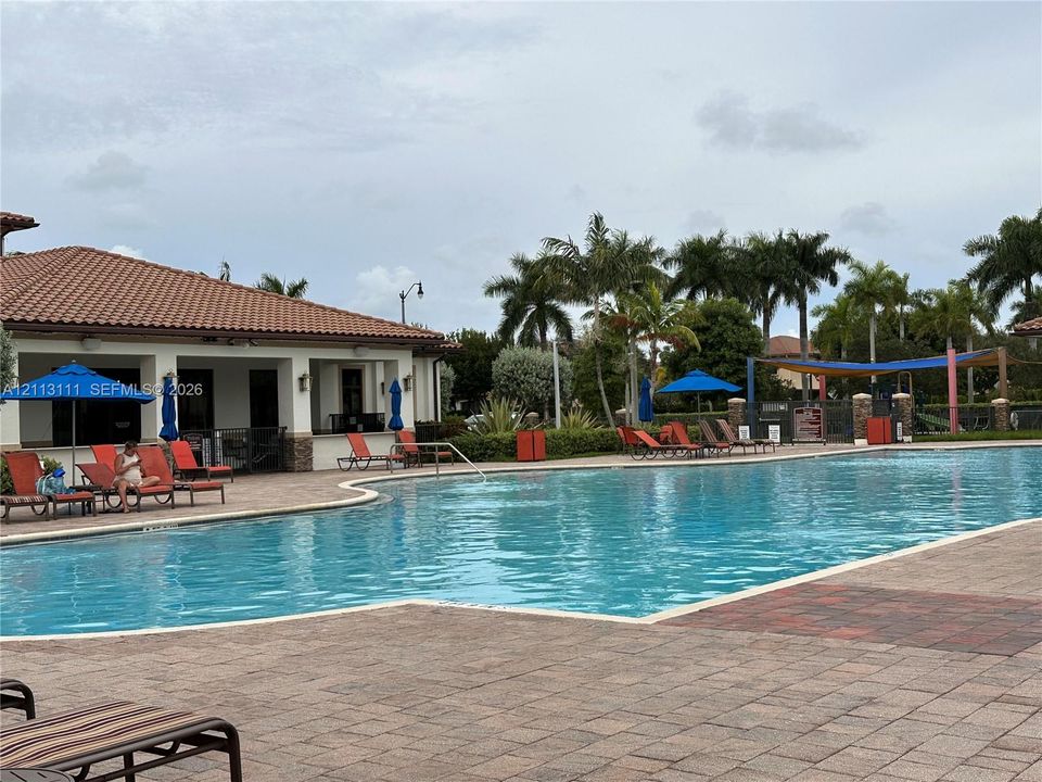 Community swimming pool featuring a paver deck, terracotta tile roof clubhouse, and mature palm landscaping