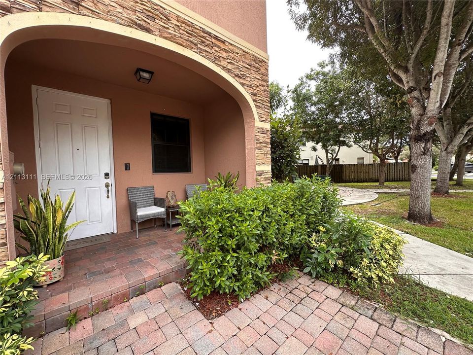 Covered entryway featuring an arched stucco facade, stone veneer accents, and brick paver porch flooring