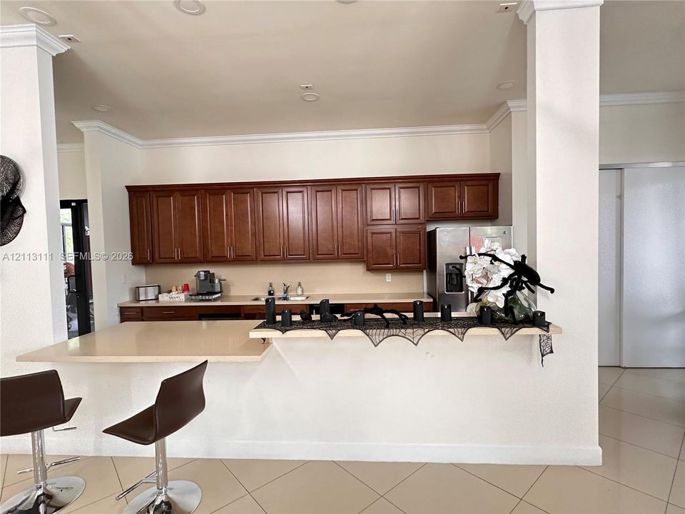 Raised breakfast bar featuring a solid-surface countertop, medium-toned wood cabinetry, recessed lighting, and tile flooring