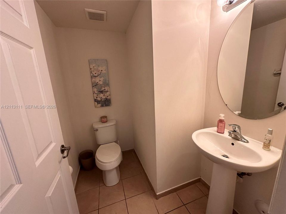 Powder room featuring a white pedestal sink, chrome faucet, oval wall-mounted mirror, and tile flooring