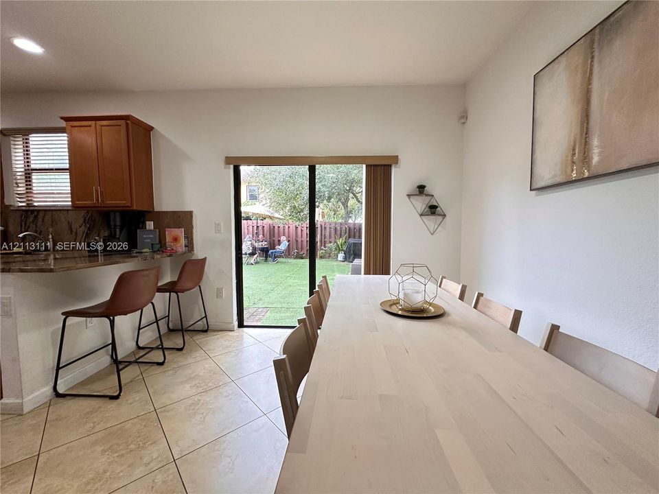 Ceramic tile flooring, stone-finished breakfast bar, recessed lighting, and sliding glass door with integrated vertical blinds