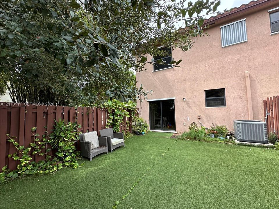 Fenced backyard featuring synthetic turf, stucco exterior siding, and sliding glass door access