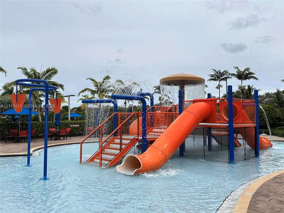 Aquatic play area featuring a multi-level structure with integrated slides, overhead water features, and a shallow-entry pool with paver decking