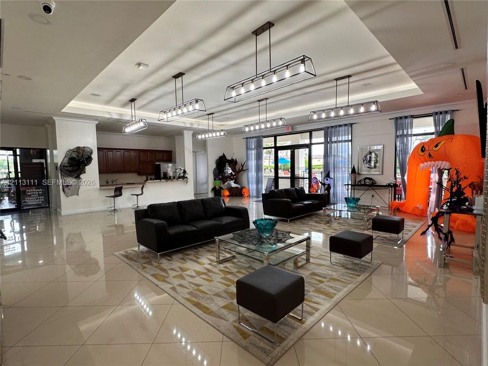 Open-concept room featuring large-format tile flooring, recessed tray ceiling, multiple rectangular linear chandeliers, and built-in cabinetry with a countertop bar