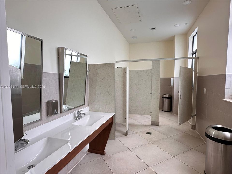 Restroom featuring a double vanity with an integrated countertop, stainless steel fixtures, wall-mounted mirrors, and tiled flooring
