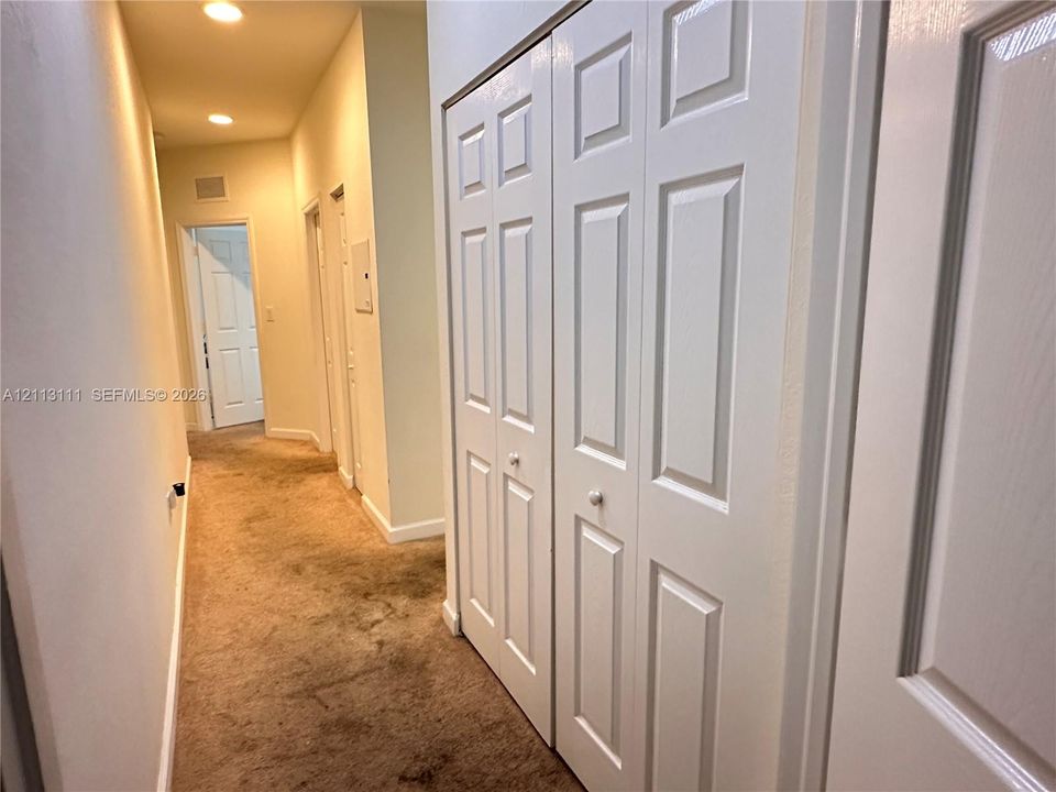 Hallway featuring recessed ceiling lighting, wall-to-wall carpeting, and white six-panel closet doors with spherical hardware