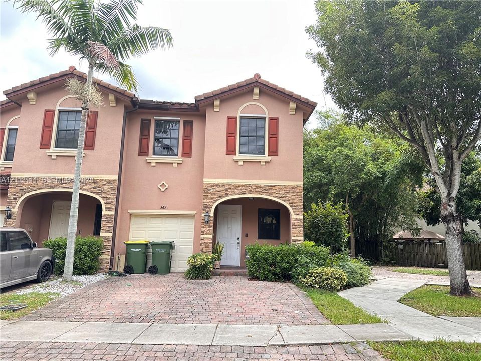 Stucco exterior featuring stacked-stone accents, decorative red window shutters, arched entryways, and a brick-paver driveway