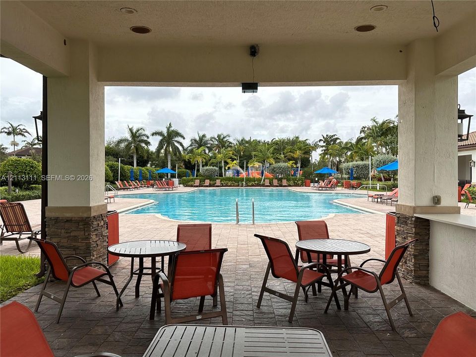 Covered outdoor patio with stone pillar accents, recessed lighting, and built-in serving counter, overlooking a paved pool deck and swimming pool