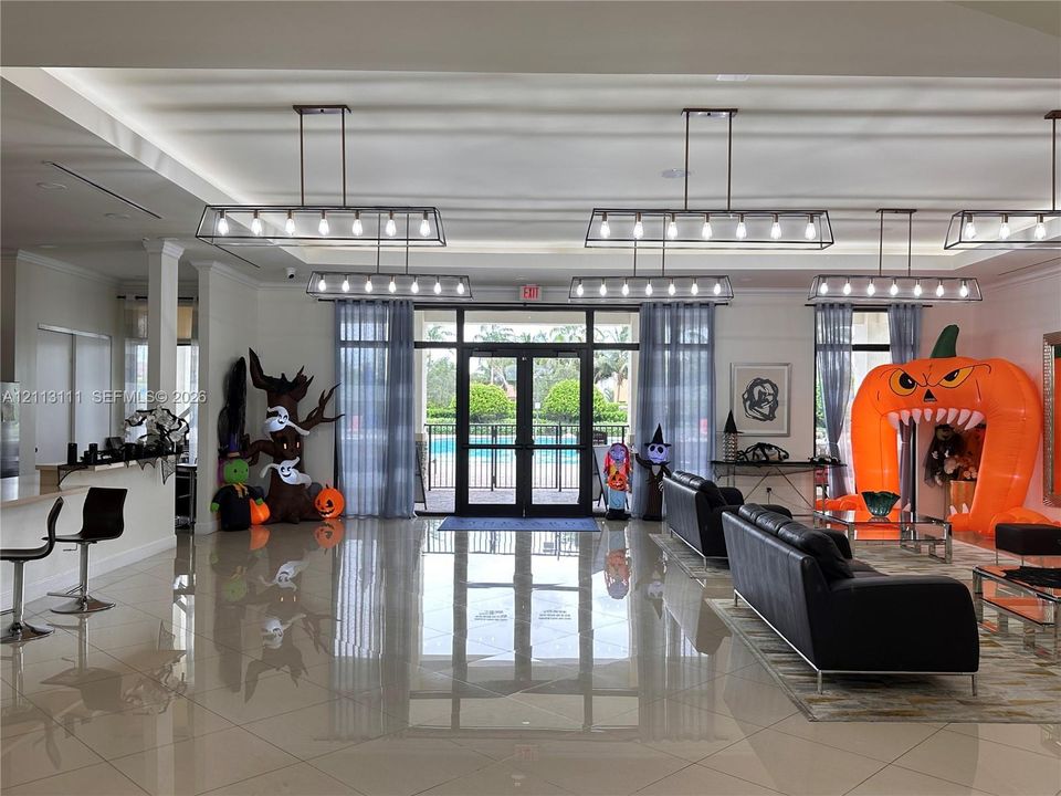 Open-concept common area featuring high ceilings, polished tile flooring, industrial-style linear pendant lighting, and full-height glass double-entry doors