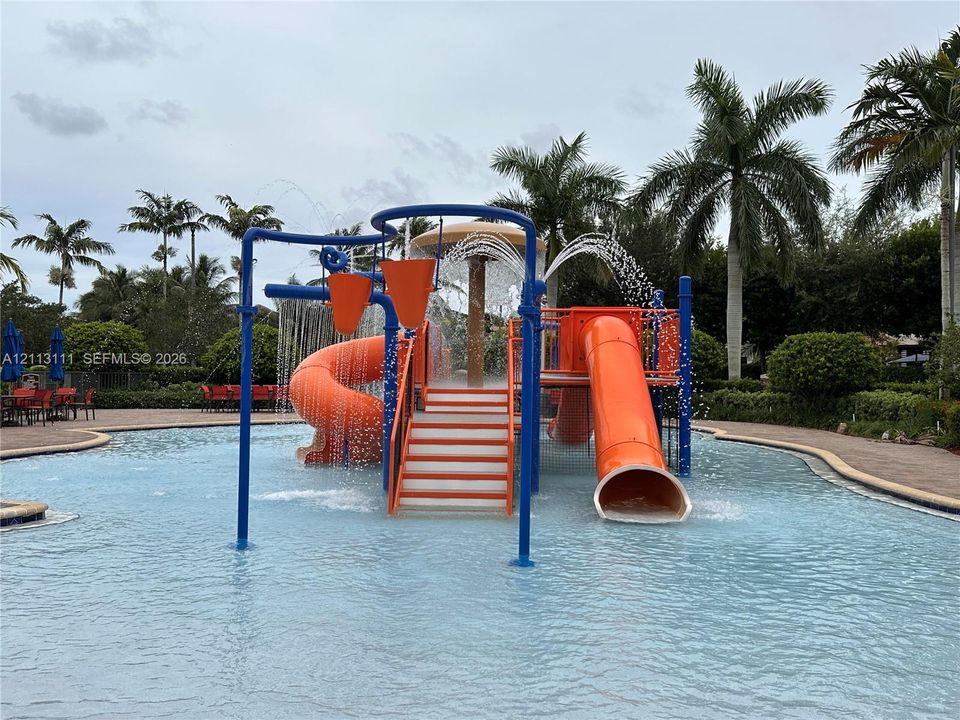 Zero-depth entry swimming pool featuring a built-in play structure, dual water slides, overhead water buckets, and perimeter paver decking