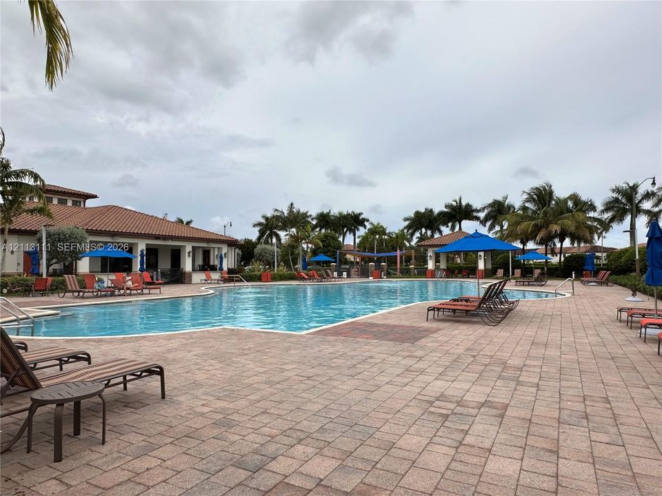 Swimming pool featuring a paver stone deck, tile-roof clubhouse, and surrounding mature palm trees
