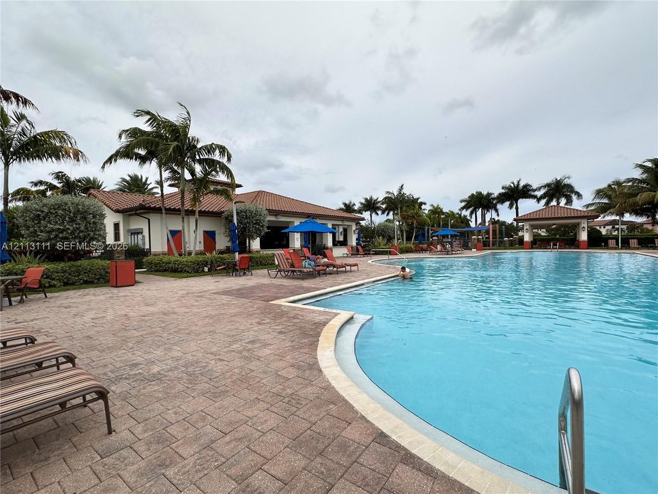 Swimming pool with a paved deck, surrounding palm trees, and a shaded pavilion