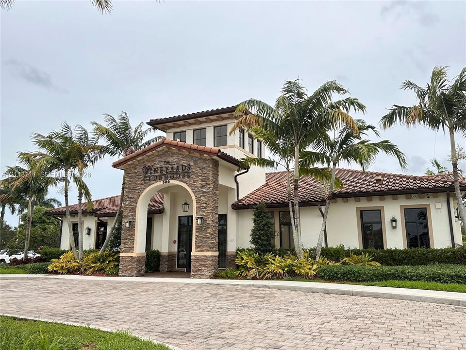 Clubhouse exterior featuring a stone-clad arched entryway, stucco facade, clay tile roof, and a paver driveway