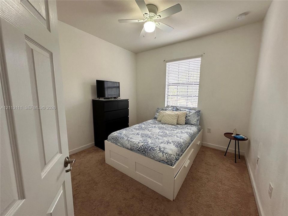 Neutral-toned wall finish, wall-to-wall carpeting, window with slatted blinds, and ceiling fan with integrated lighting