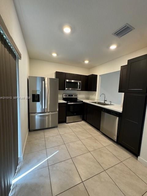 Kitchen featuring dark cabinetry, stainless steel appliances, solid-surface countertops, and ceramic tile flooring